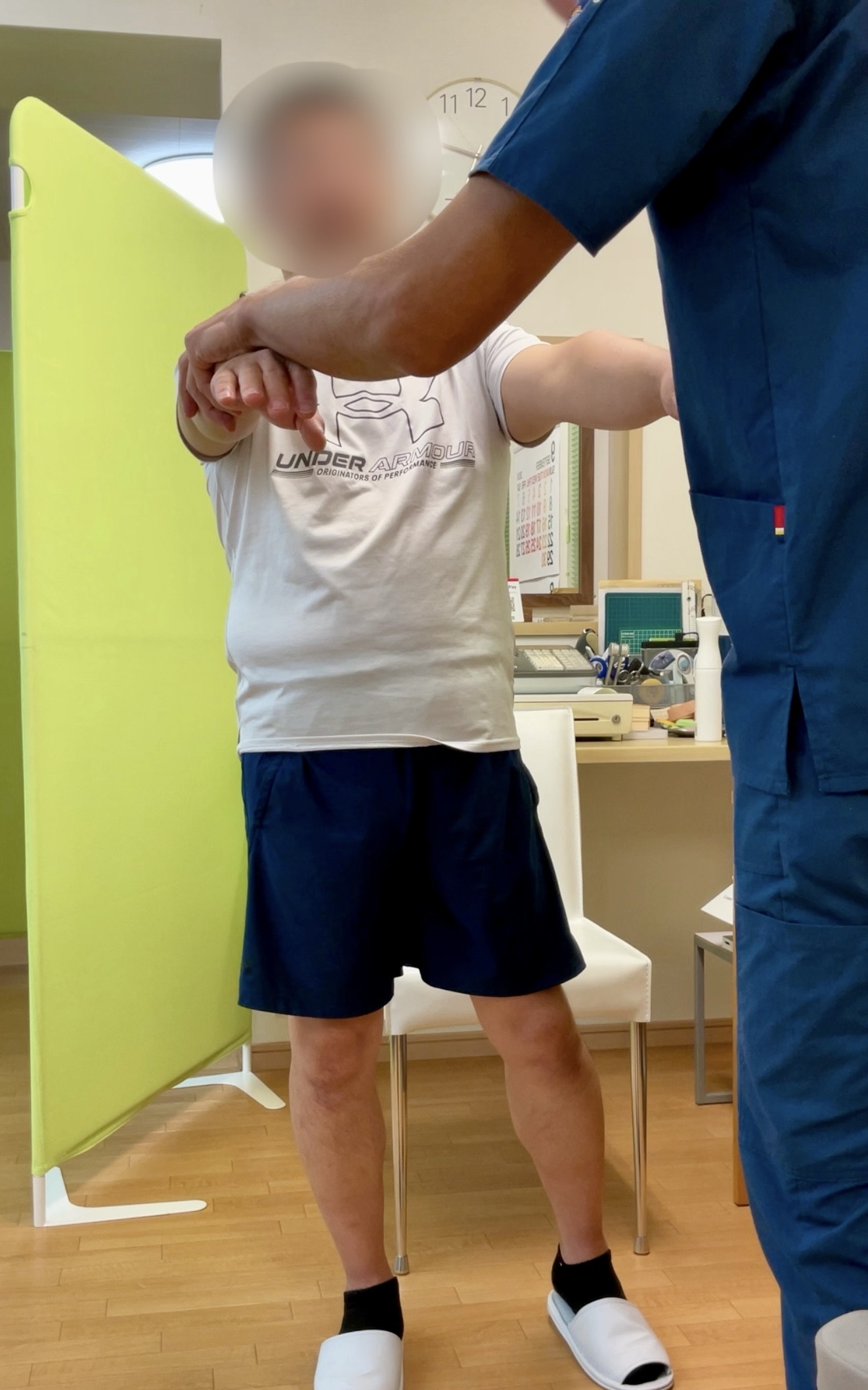 立位で施術者がKさんの腕の筋出力や神経反射の状態を確認している検査中の様子。